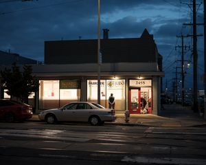 Illuminated storefront with parked car on dark urban street at night.