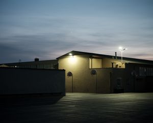 Industrial building exterior with bright security light in empty parking lot at dusk.