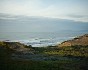 Dramatic coastal landscape with waves crashing against rocky cliffs under cloudy sky.