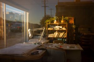 Sunlit desk by window with books and bottles creating warm atmospheric scene.