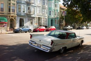Vintage car parked on street with colorful Victorian row houses in San Francisco.