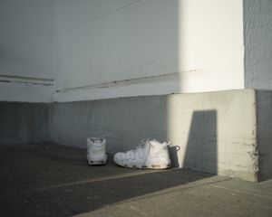 White sneakers sitting in corner of concrete space with dramatic shadow and light.