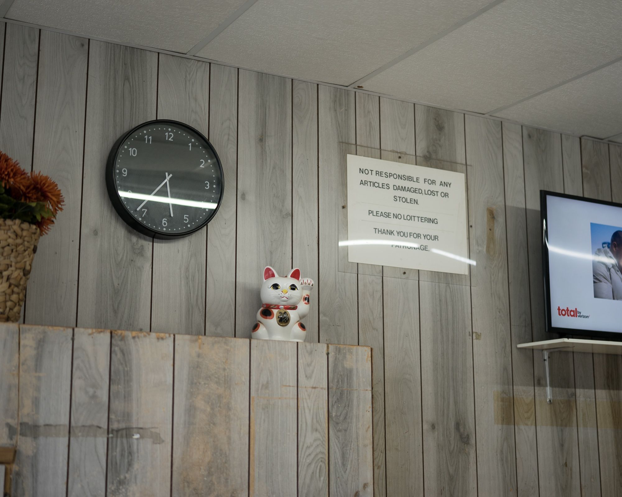 A white maneki-neko lucky cat figurine and clock mounted on a wood-paneled wall.