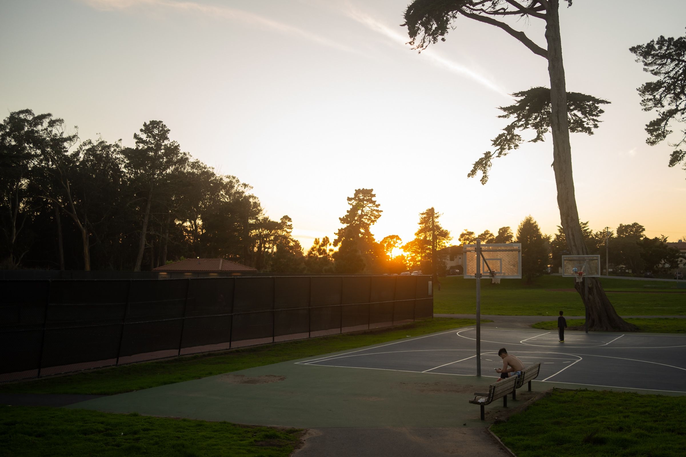 Sunset view of a tennis court and trees silhouetted against an orange sky.