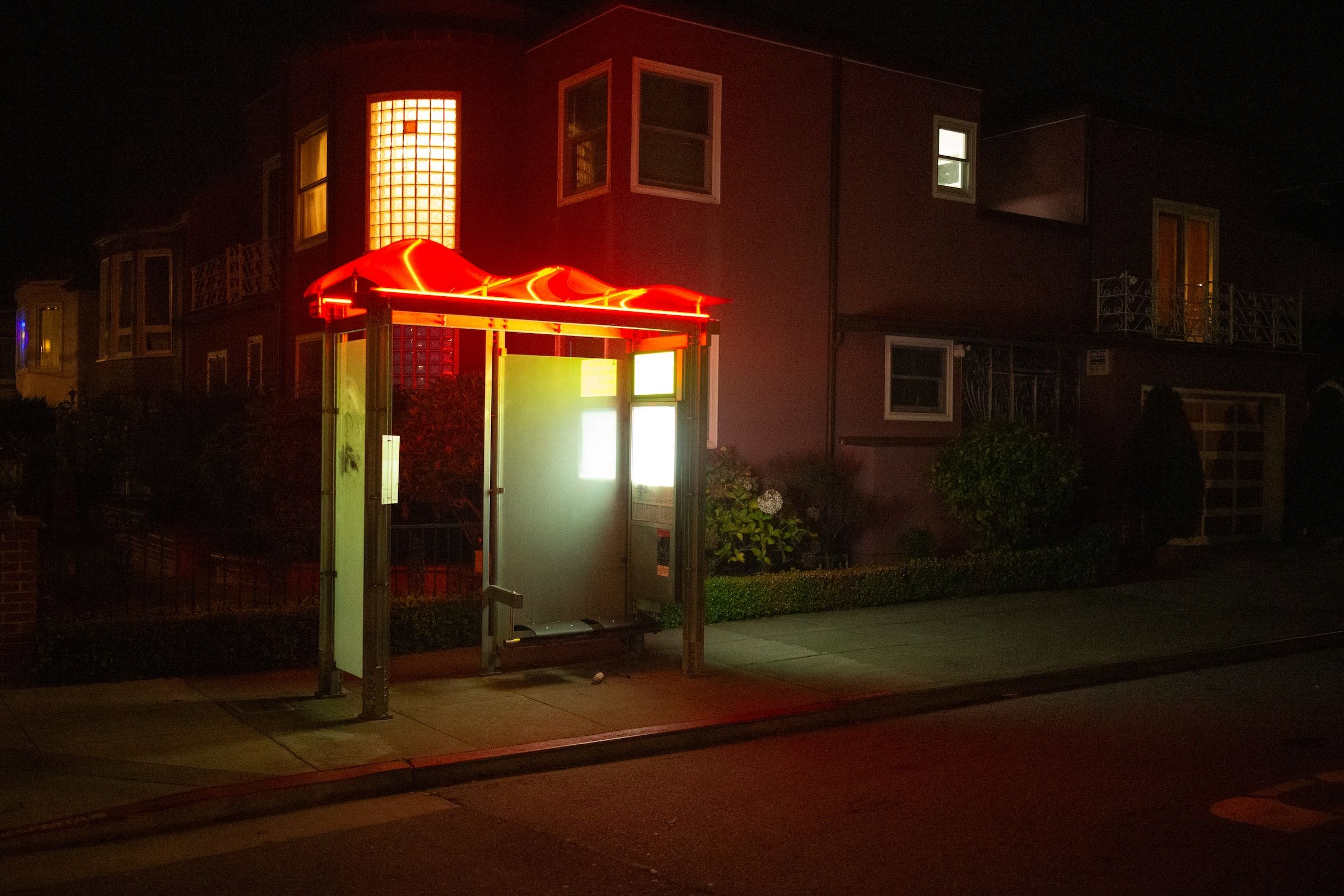 Illuminated red phone booth glowing at night on a dark residential street corner.