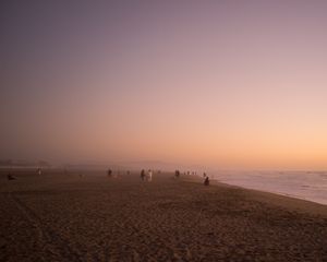 Misty beach at sunset with silhouettes of people walking along the shoreline.