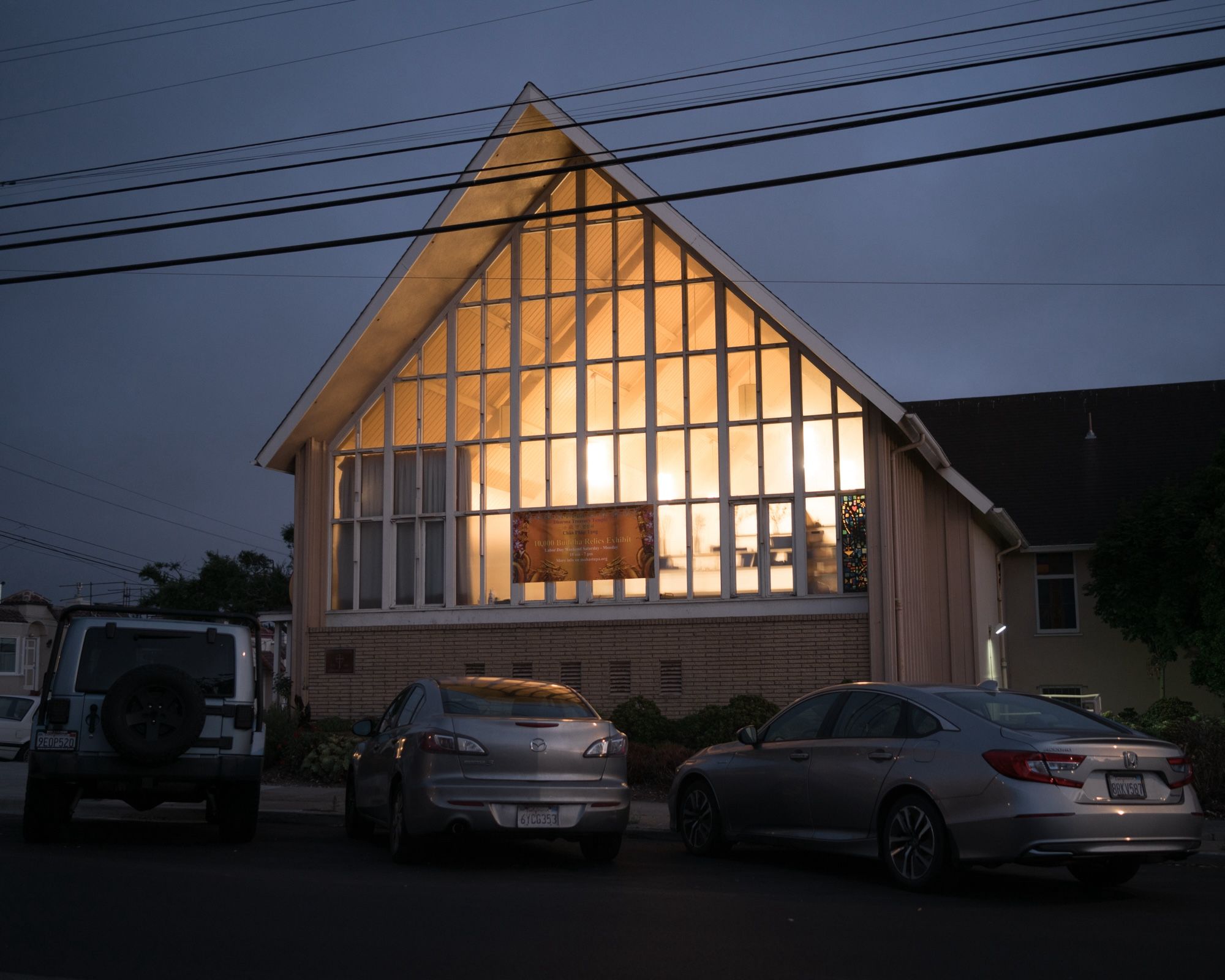 A-frame building with glowing windows at dusk with parked cars in the foreground.