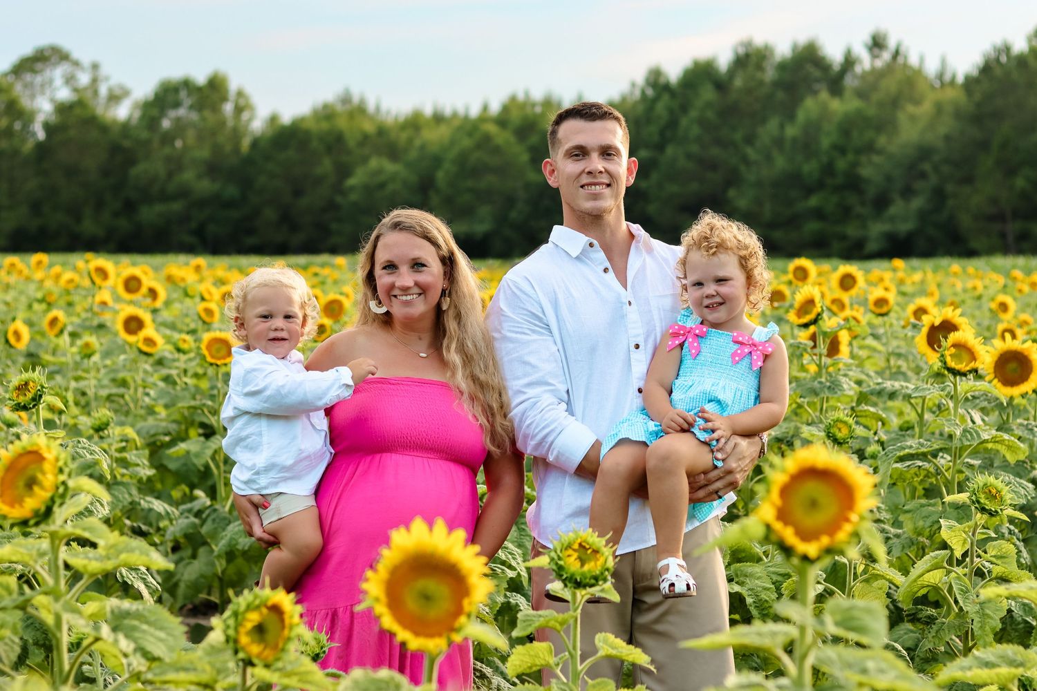Family of four poses together in vibrant sunflower field during summer photo session.