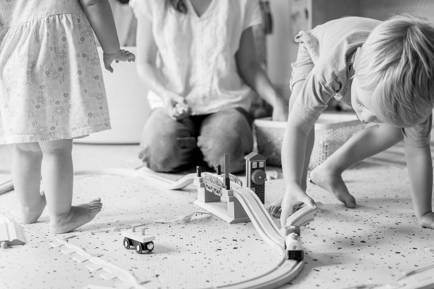 Children playing with a toy race track setup on the floor in black and white.