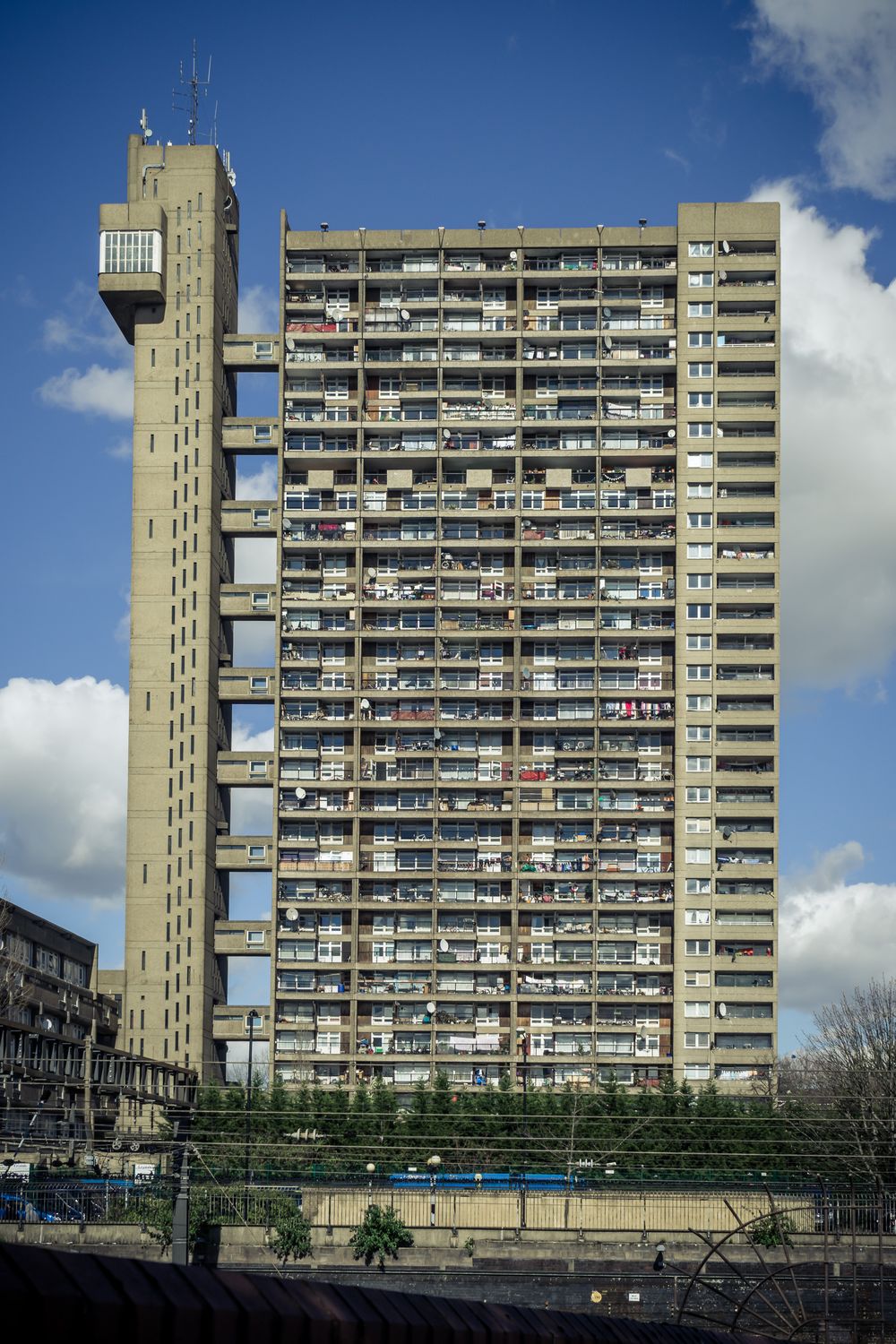 Row of identical high-rise apartment buildings with balconies against a cloudy blue sky in London.