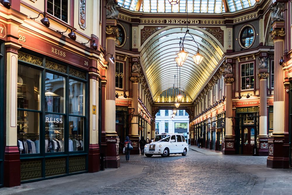 Historic Leadenhall Market arcade in London with ornate Victorian architecture and glass ceiling illuminated by natural light.