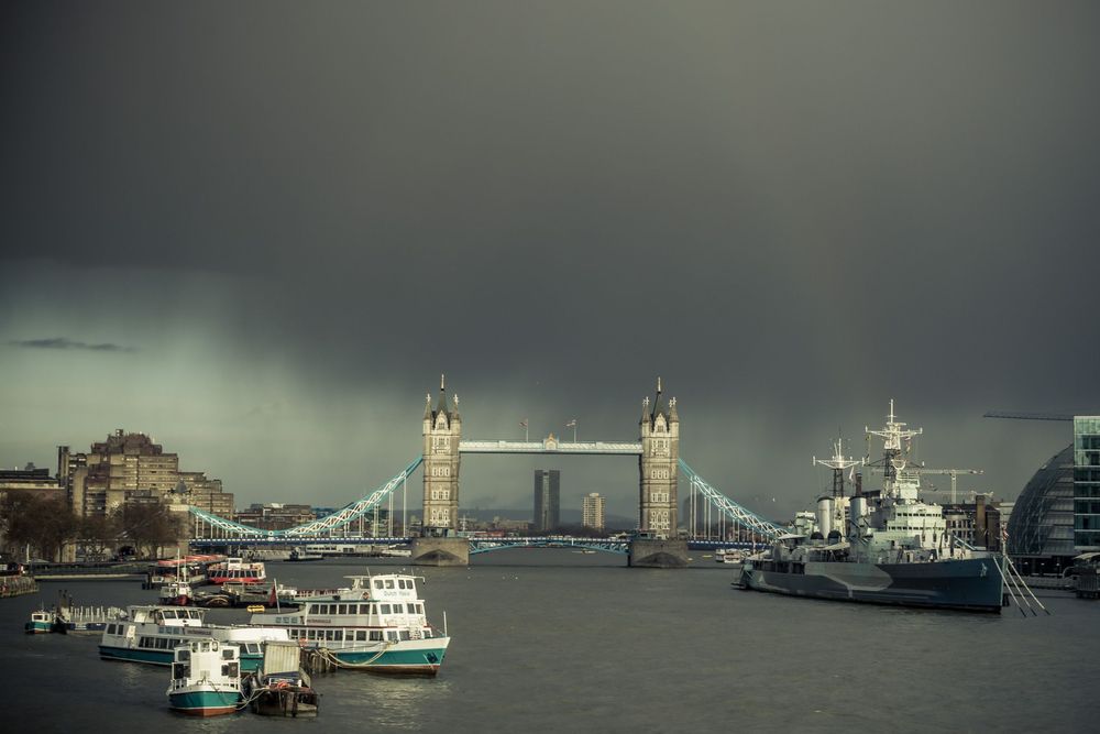 Panoramic view of Tower Bridge and the River Thames in London under dramatic stormy skies.