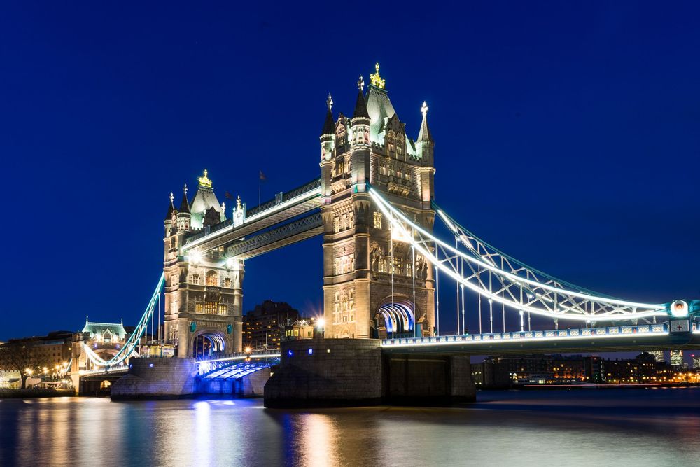 Tower Bridge in London illuminated at night with blue lights reflecting on the River Thames during long exposure.