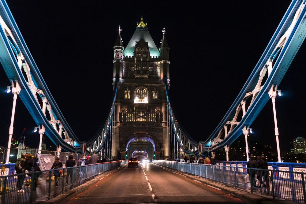 Architectural lights illuminate Tower Bridge at night reflecting on the River Thames in London.