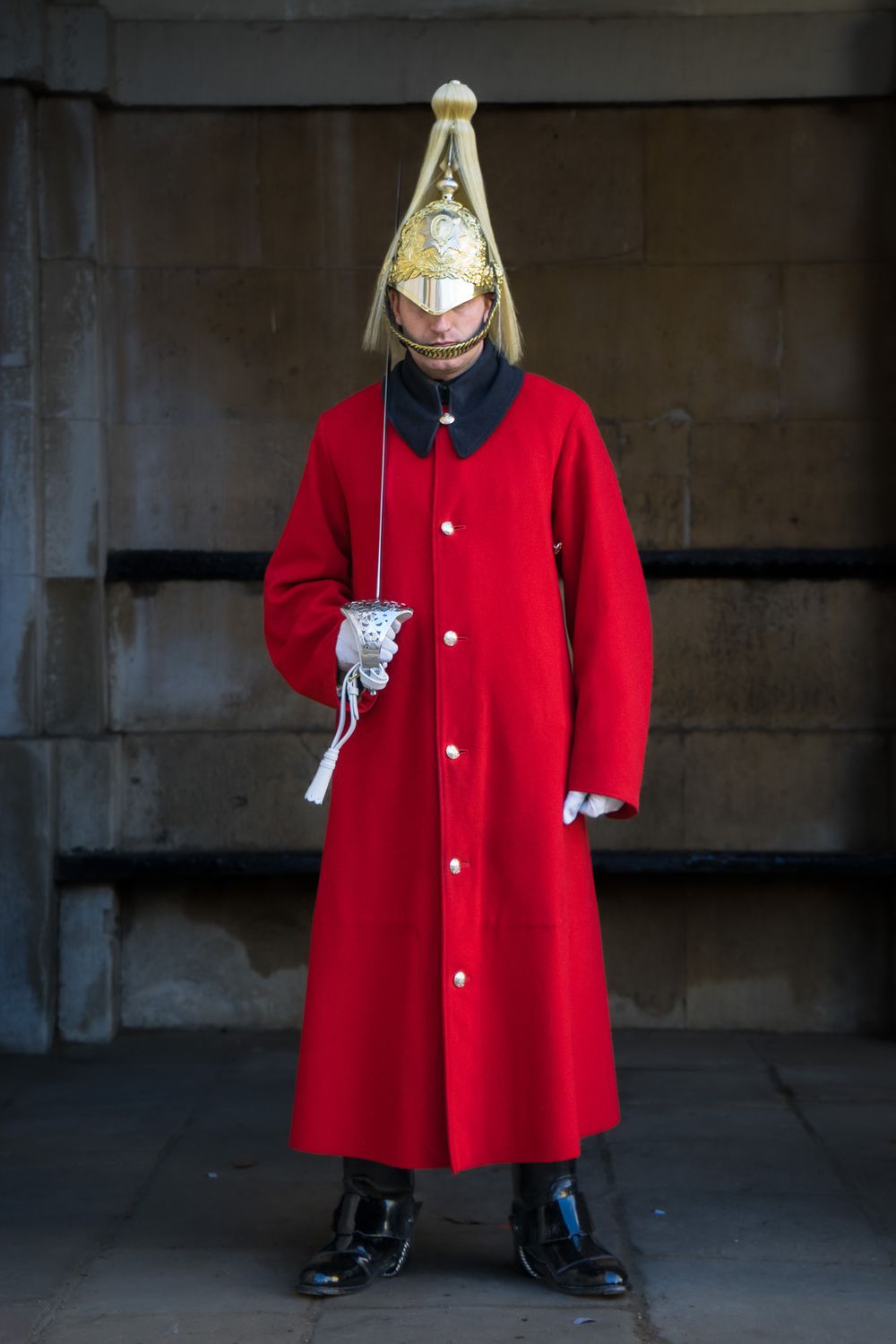 A bright red wool swing coat with silver buttons displayed on a fashion mannequin against a dark wall.
