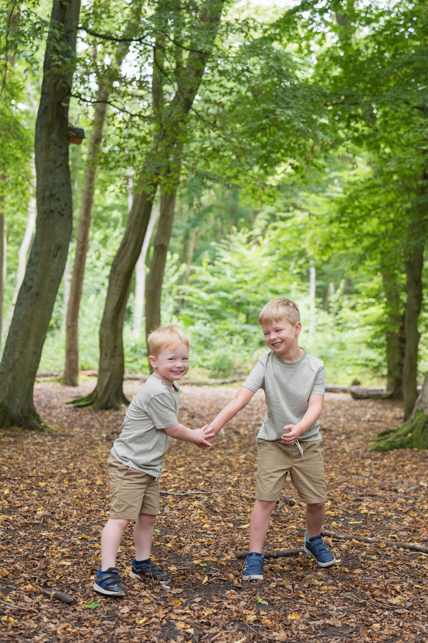 A family enjoys a playful moment together while posing for photos in a wooded forest setting with fallen leaves.