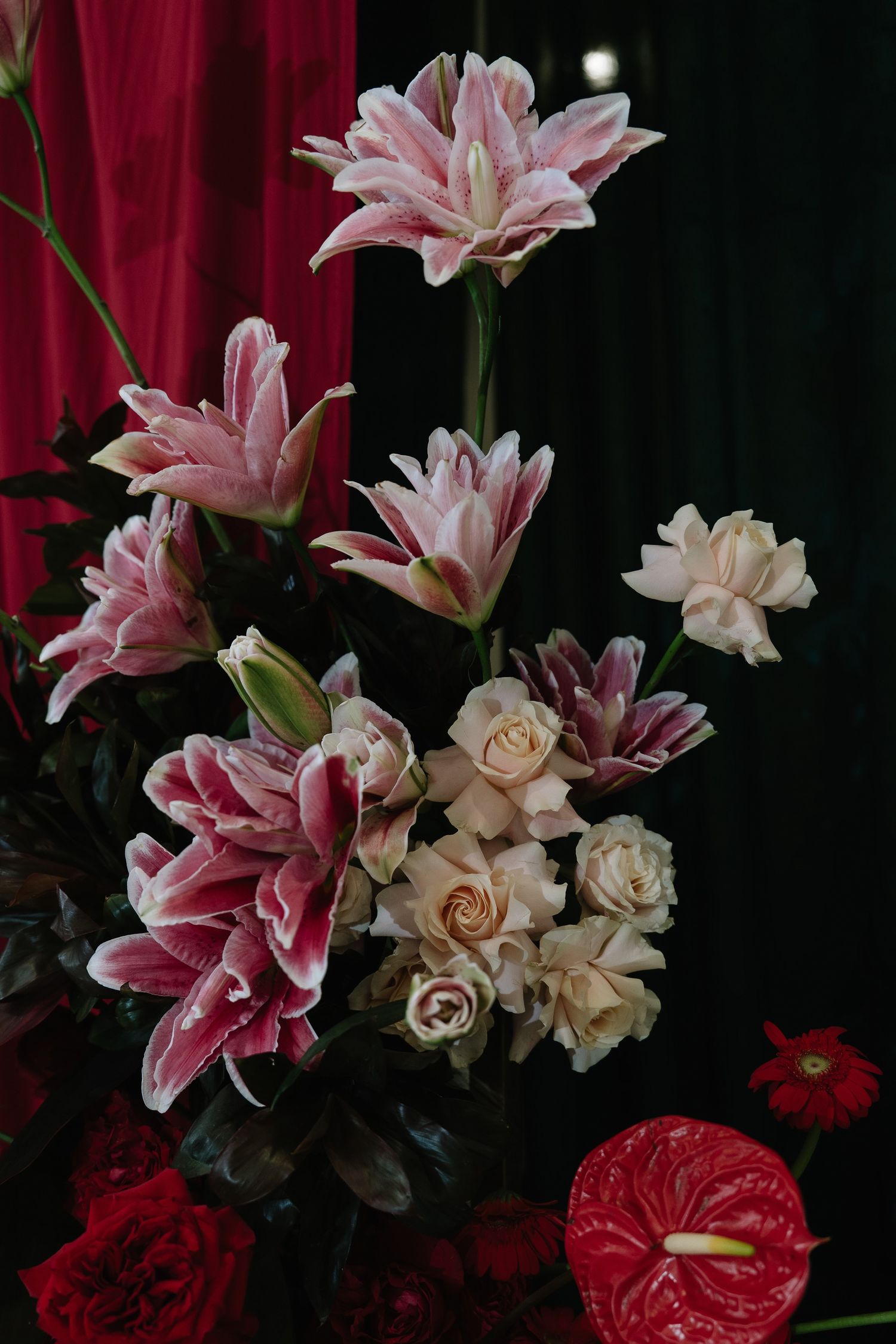 Pink stargazer lilies and cream roses arranged with red anthurium in an elegant floral display.