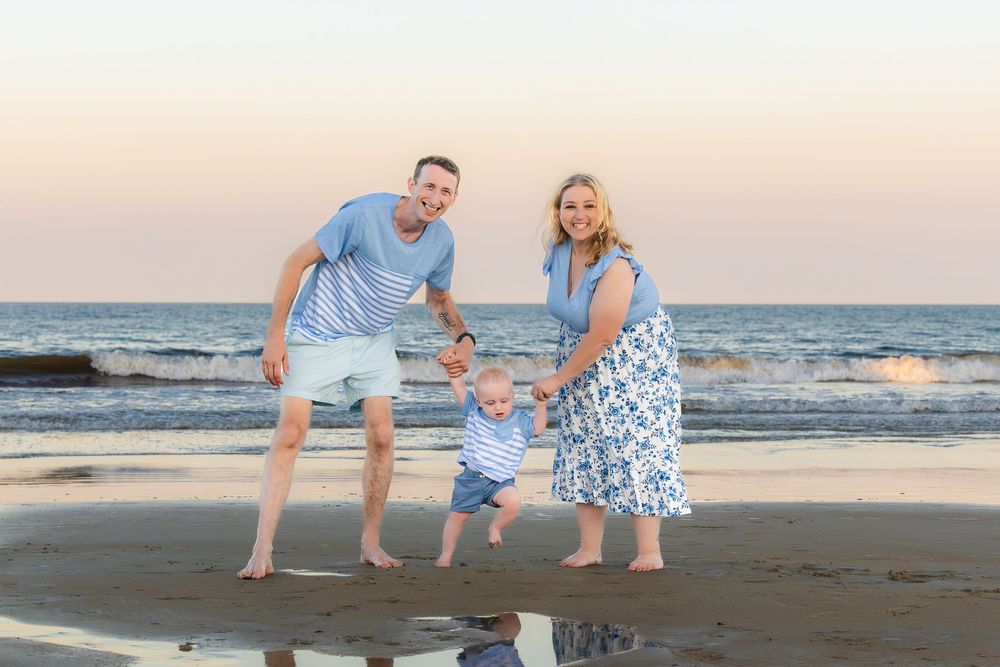 Family enjoying a beach sunset while playing and walking together in matching blue and white outfits.