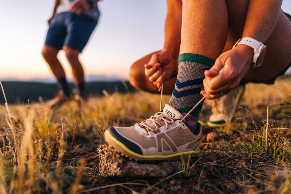 Group of people's feet in sneakers and hiking boots resting together in golden grass at sunset.
