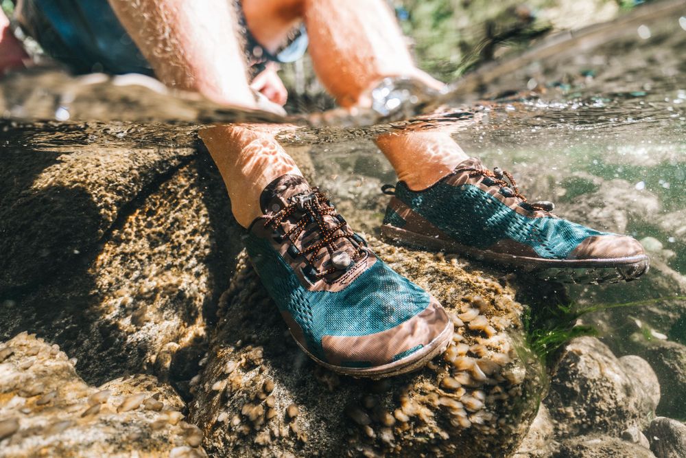 Leather hiking boot stepping into a puddle of water on a rugged mountain trail during an outdoor adventure.