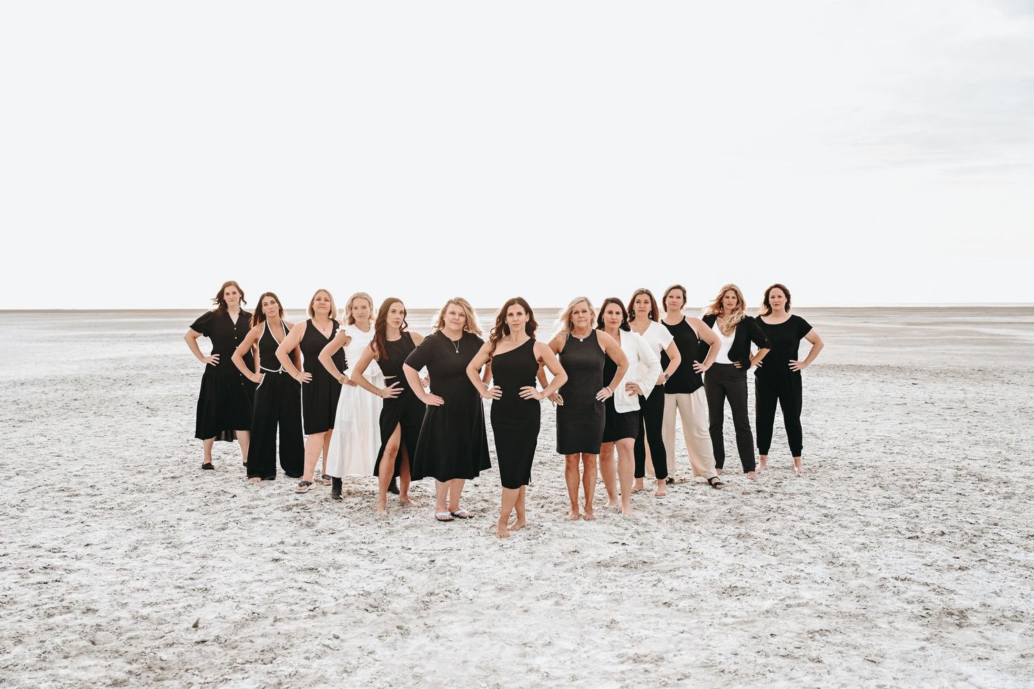 Group beach photo featuring people wearing black outfits standing on white sand.