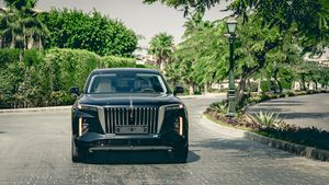 Luxury black car photographed in front of Mediterranean-style architecture and palm trees.