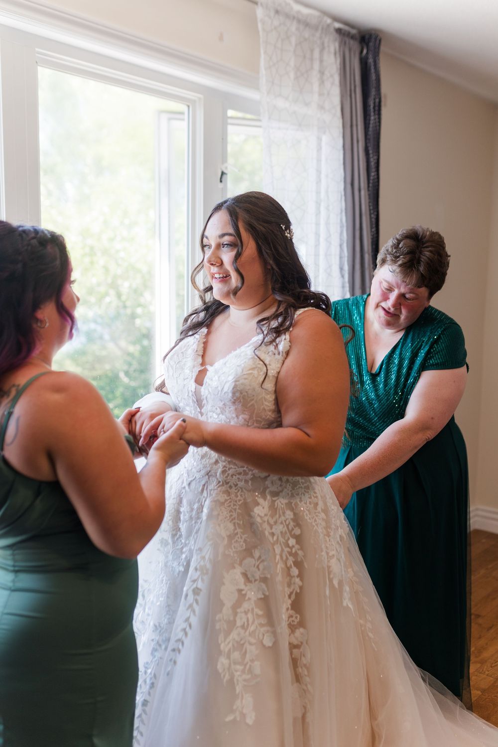 A sequence of four photos showing a bride getting into her lace wedding dress with help from others in green dresses.