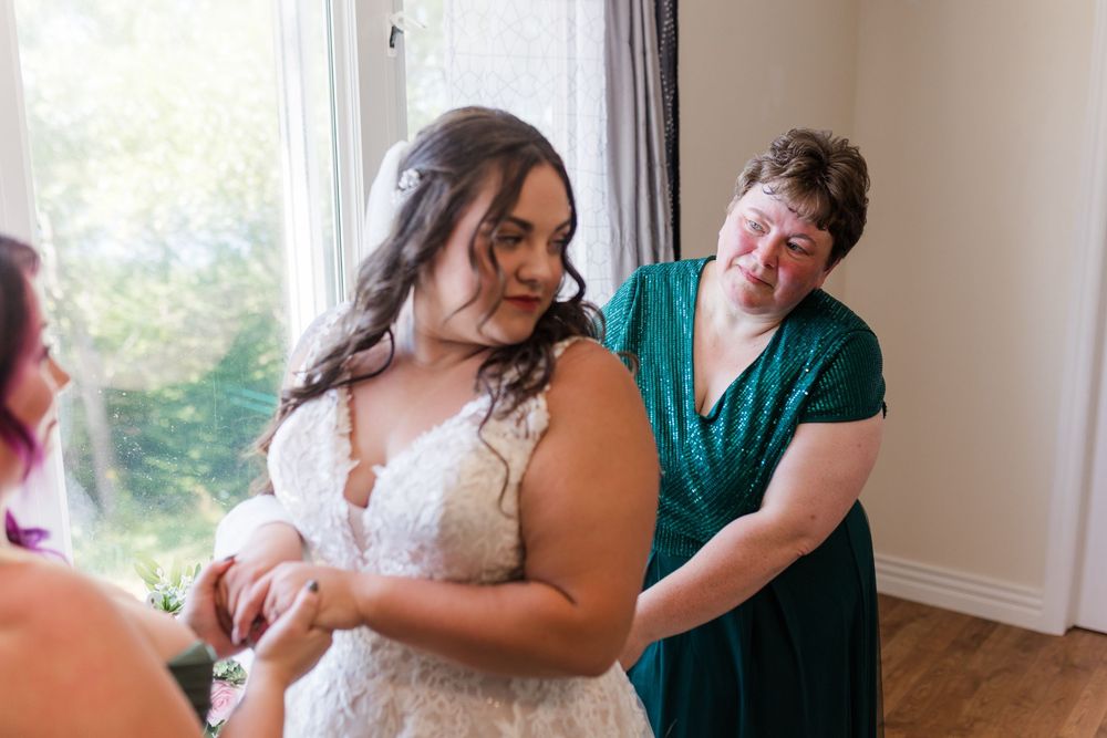 Someone helps adjust a beautiful lace wedding dress during bridal preparations in a sunlit room.