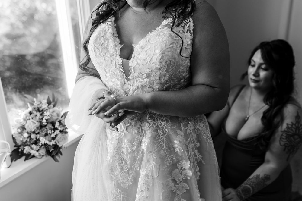 Black and white photo showing details of a delicate lace wedding dress while getting ready for the ceremony.