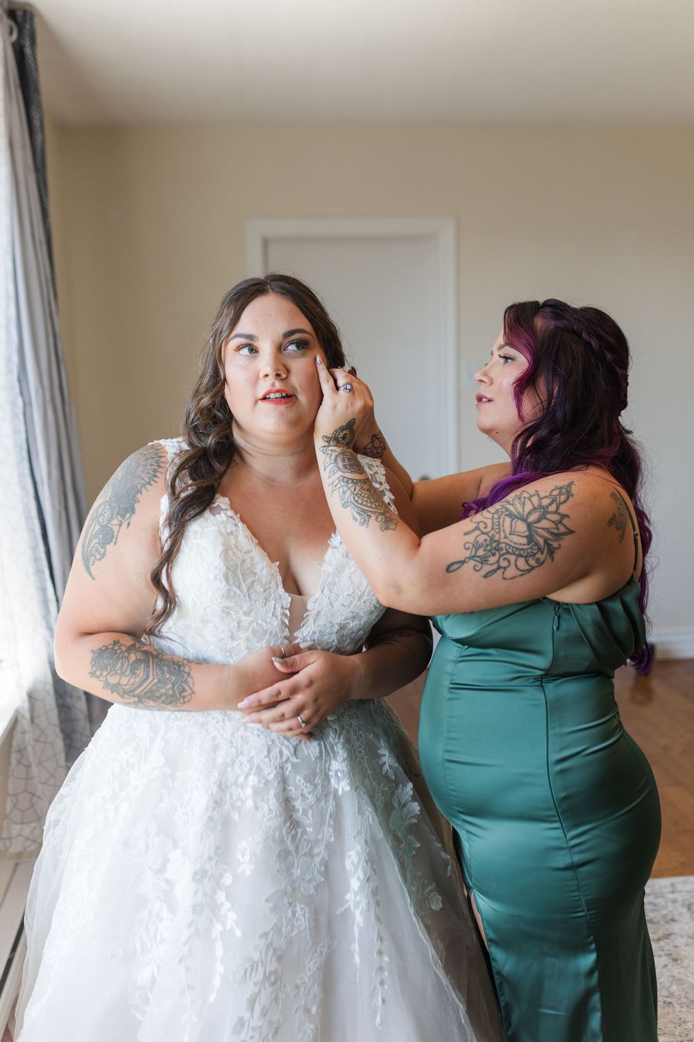 Two people in formal attire getting ready, with one wearing a white lace wedding gown and another in an emerald green dress.