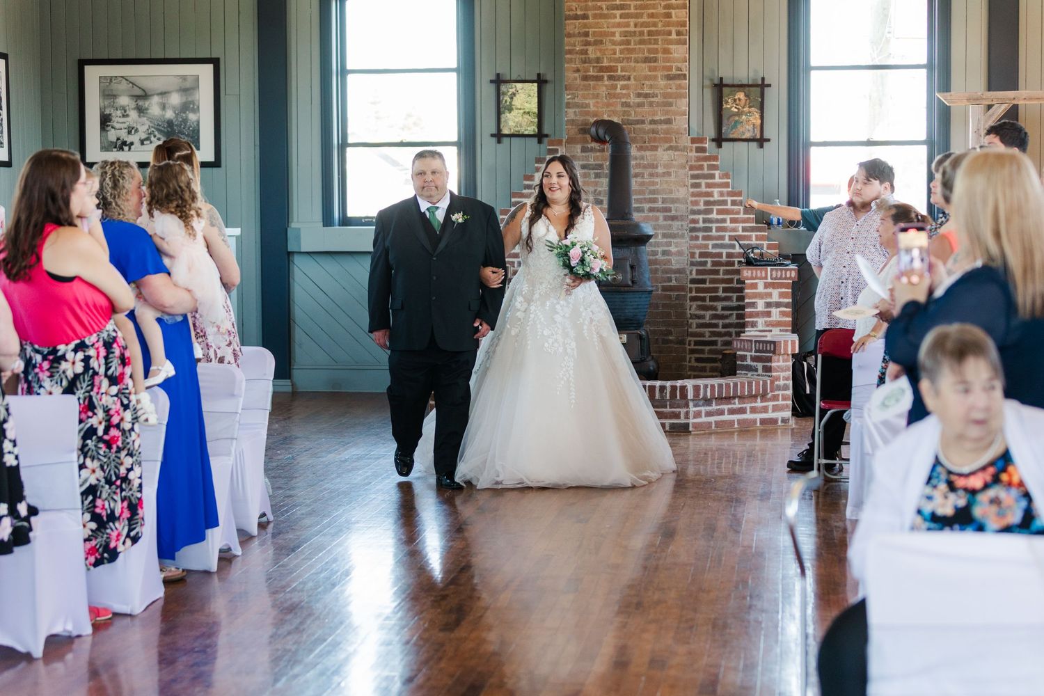 Wedding ceremony takes place in a historic venue with exposed brick walls and hardwood floors as guests look on.