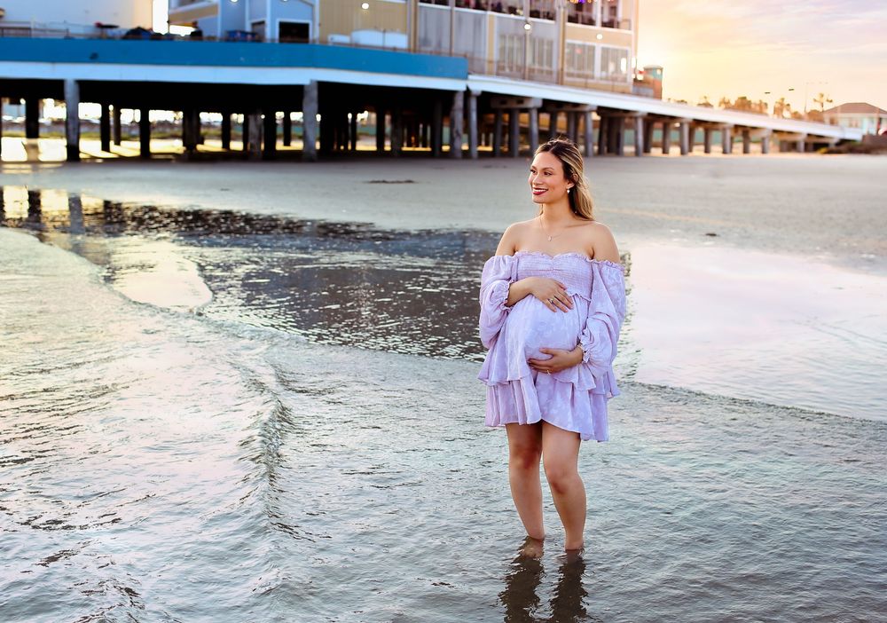 Pregnant mama posing near beach water while holding her belly