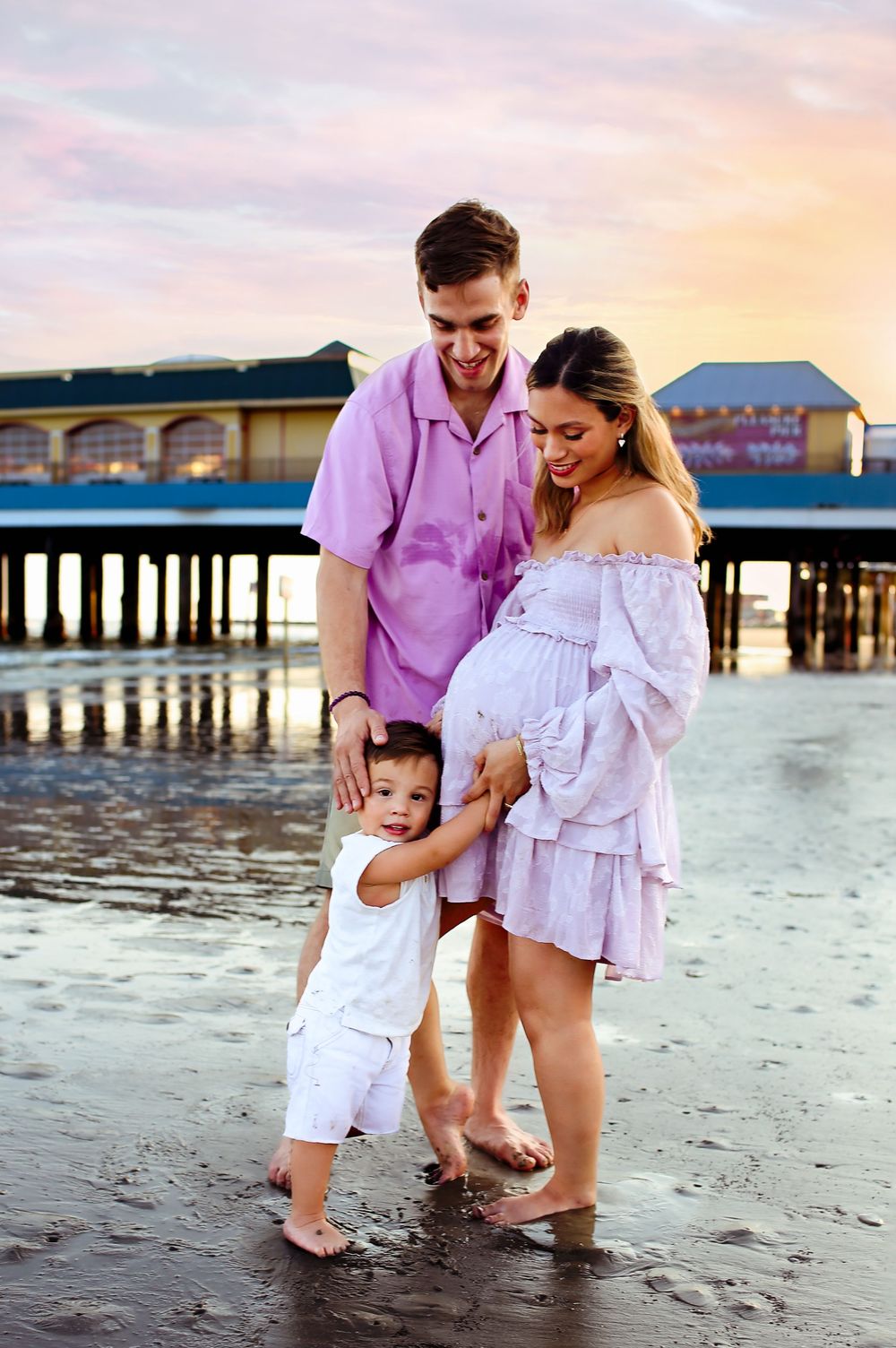 Mom, dad and oldest sun standing snuggling close on the beach while sons face is on mamas pregnant belly