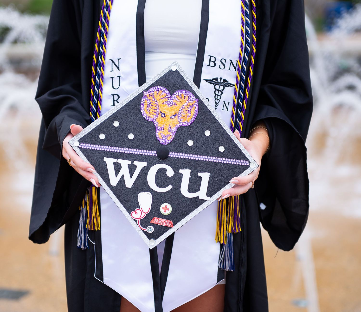 A decorated graduation cap with WCU letters and floral design shown against a black graduation gown.