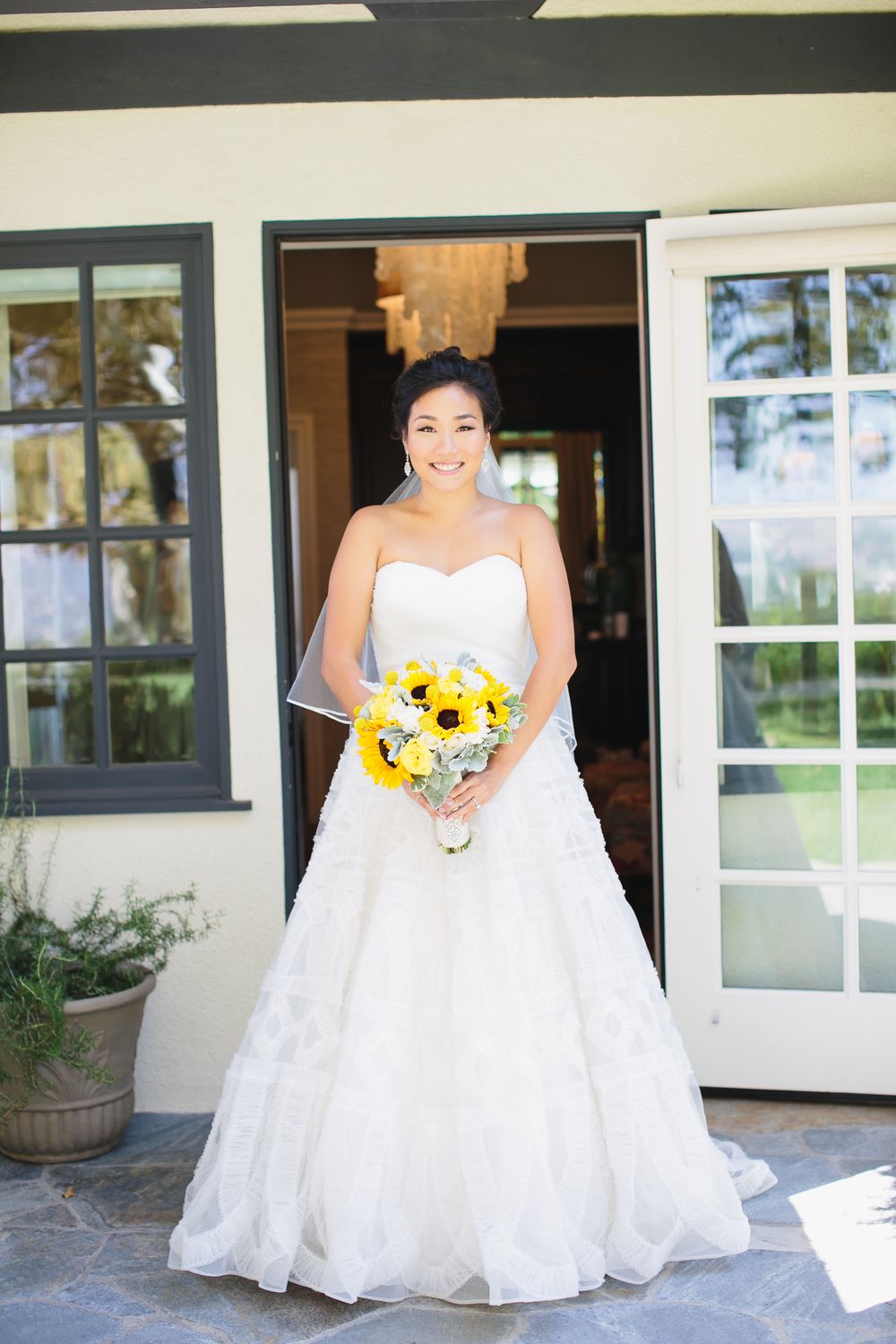 Bride in strapless wedding dress holds vibrant yellow sunflowers while sitting outdoors.
