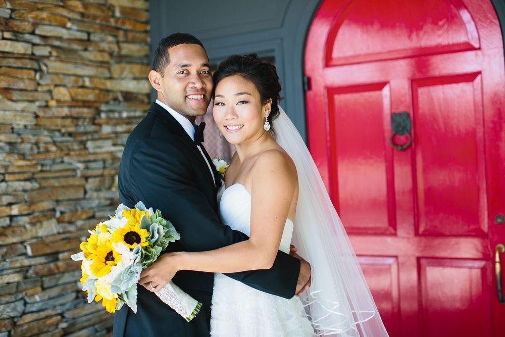 Newlyweds share intimate moment in front of large red door and stone facade.
