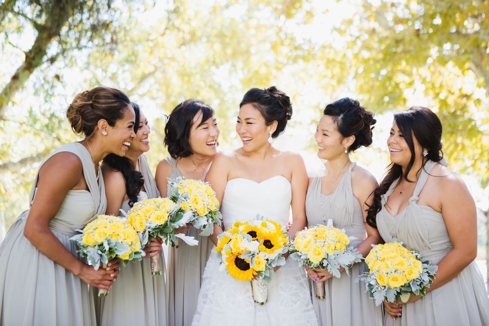 Wedding party in grey dresses holding yellow sunflower bouquets poses together outdoors.