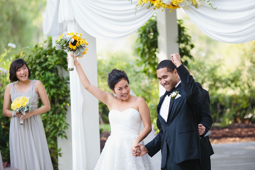 Wedding ceremony setup with white draped gazebo and bright yellow sunflower accents in outdoor garden setting.