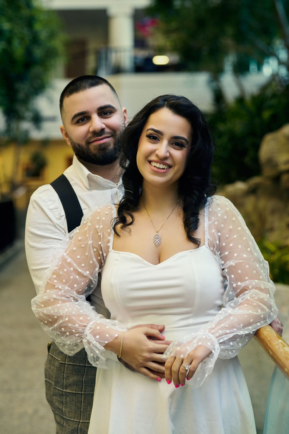 A happy couple embraces at their wedding, the bride wearing a white lace sleeved dress and groom in plaid pants and vest.