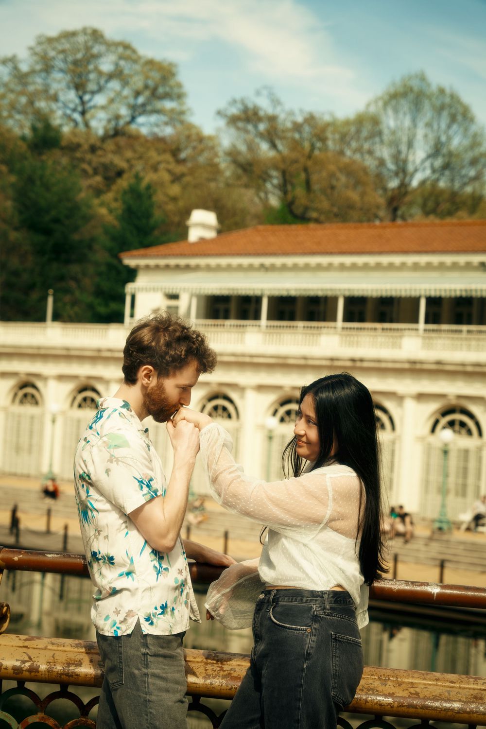 Couple shares a playful moment by lake with historic building in background at sunset. at prospect park boat house