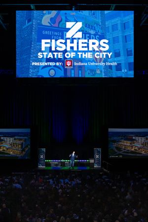Large audience gathered in a darkened auditorium with blue stage lighting and corporate branding displays.