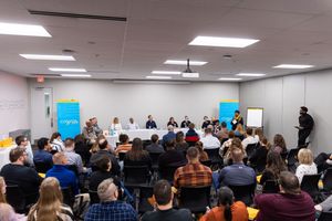 A large panel discussion event in a conference room with audience members seated in rows facing the speakers.