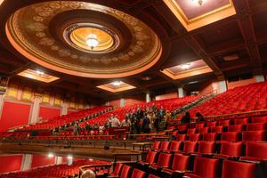 Interior view of an ornate theater with red seats and decorative ceiling featuring a large circular medallion detail.