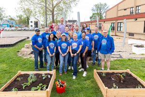 Volunteers in bright blue shirts gather around newly built garden beds outside a community building.