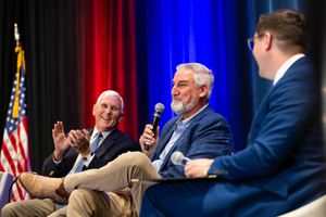 Three people sitting on stage during a panel discussion with American flag and red and blue curtain backdrop.