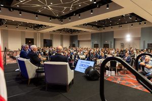 A panoramic view of a crowded conference hall with theater-style seating and modern lighting fixtures on the ceiling.