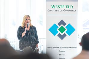 A speaker presents at a Westfield Chamber of Commerce event with a banner and audience visible in the background.
