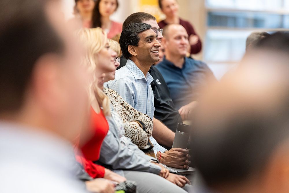 Members of an audience smile and laugh while enjoying a presentation in an indoor venue.