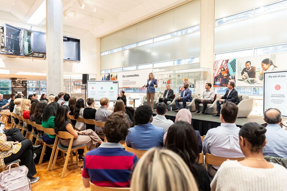 Large audience sits in chairs watching a presentation or workshop in a bright indoor retail or commercial space.