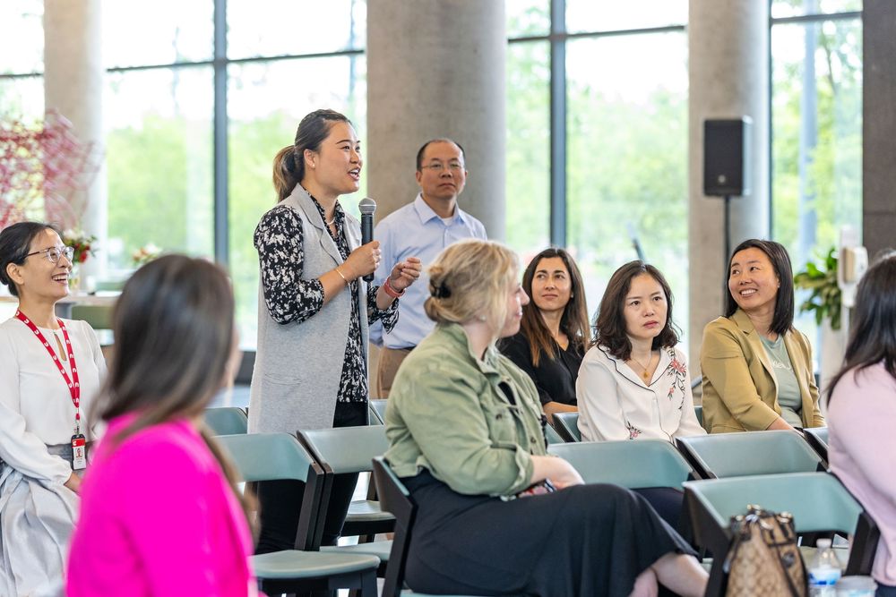 A diverse group of people participate in a professional seminar or meeting in a bright room with large windows.